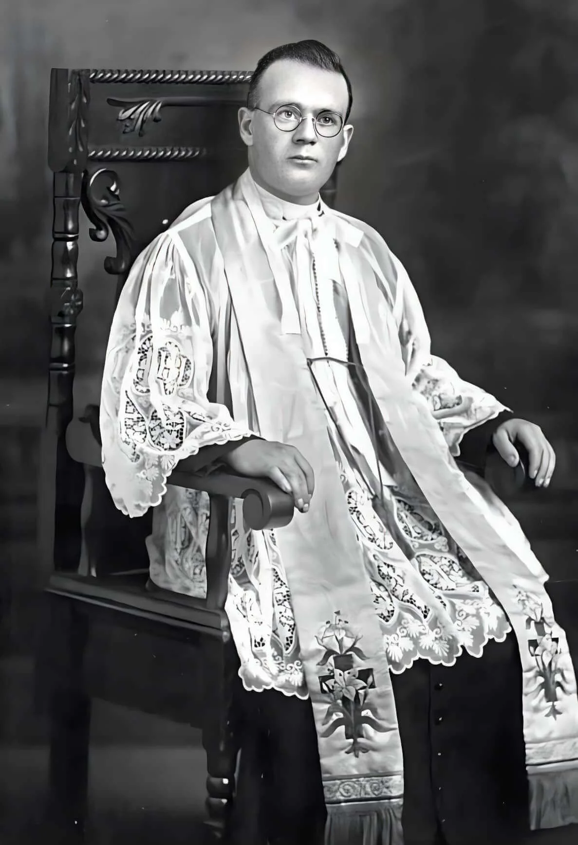 El Padre Arthur Gallant en adornos sacerdotales, sentado en una silla